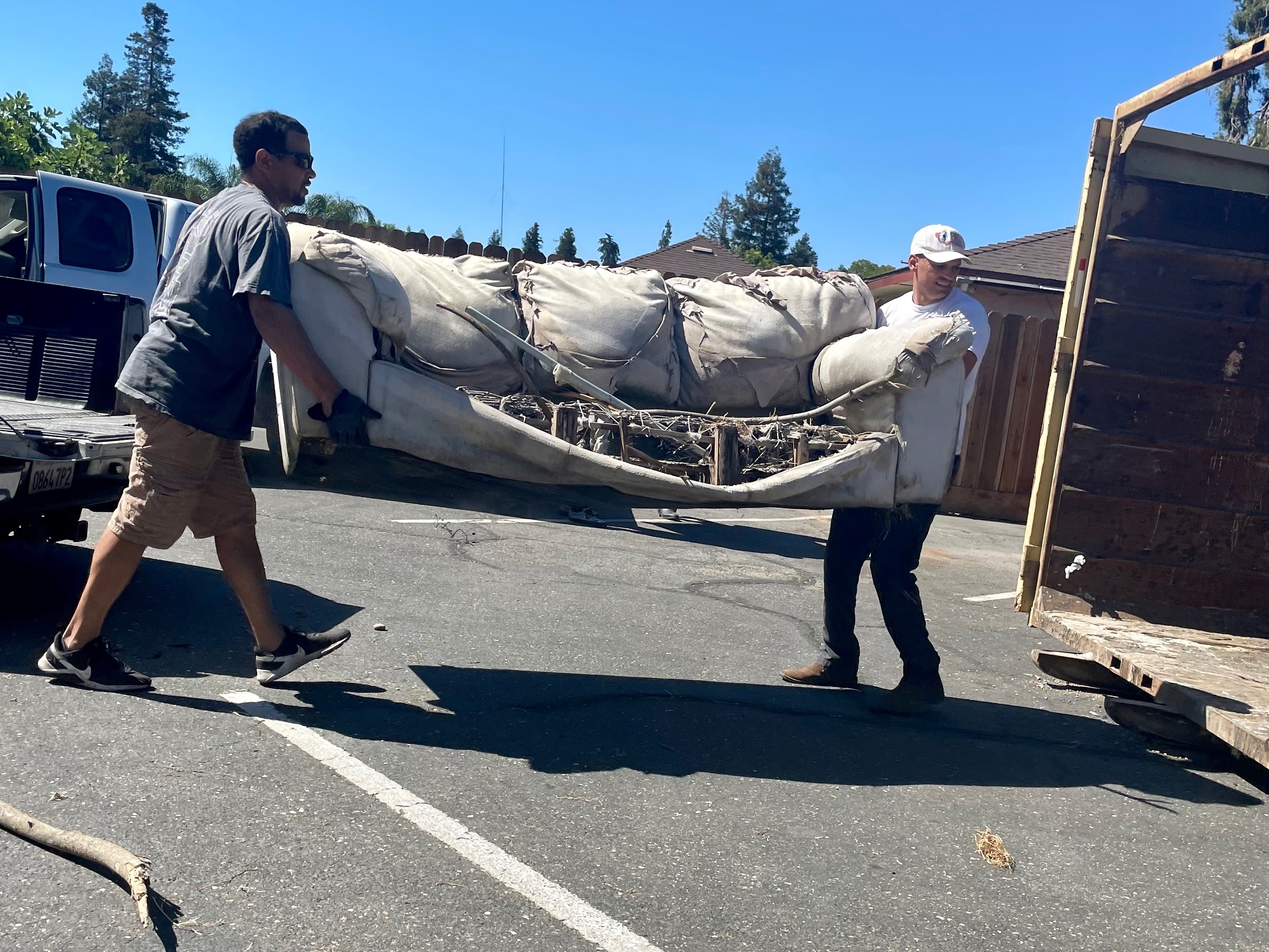 Channce Condit helping another man carry an old broken couch into a dumpster trailer during the Empire Community Cleanup Day in 2022