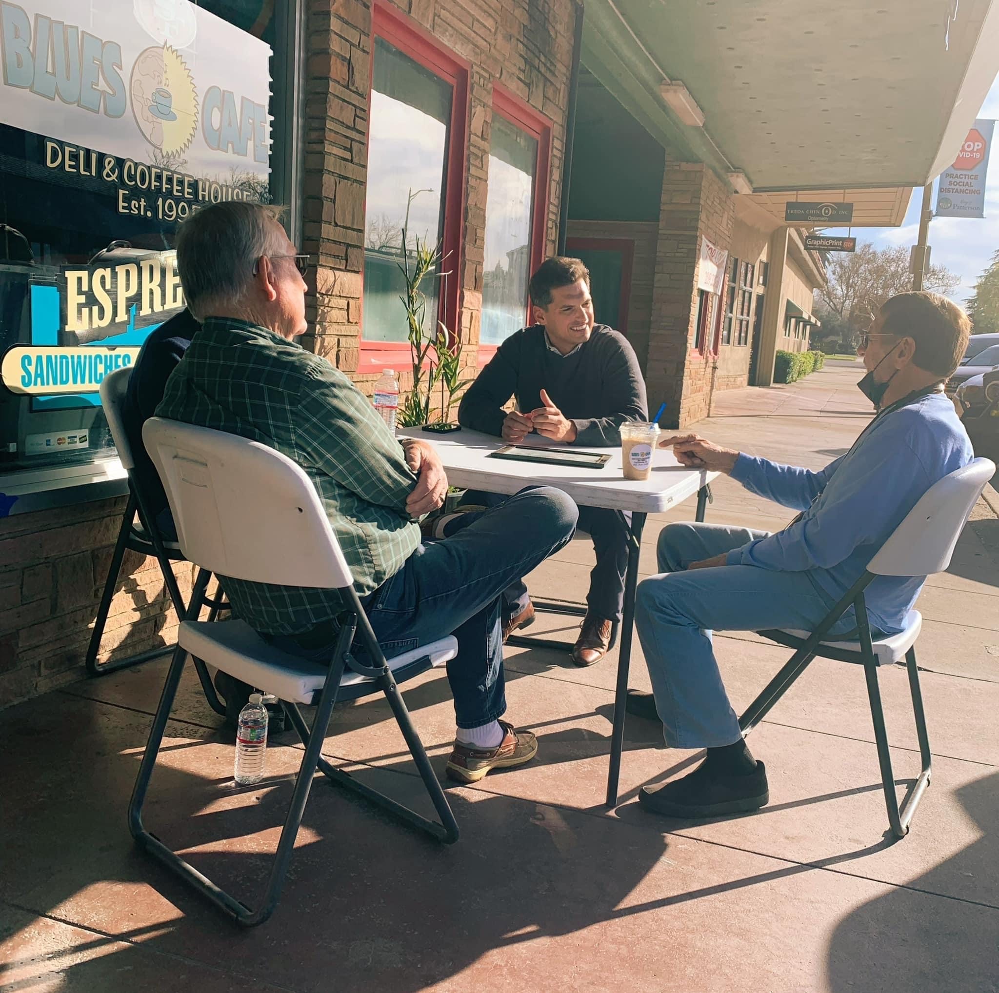 Channce Condit at a table outside of a local store front having a discussion with three men during the Patterson District Office Hours in 2022